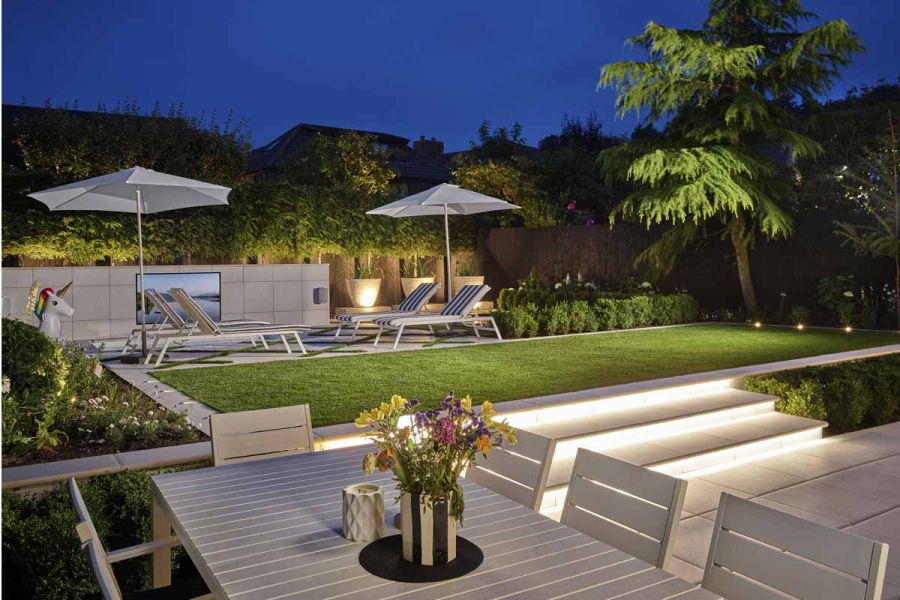 Outdoor dining table facing a grass area running into an outdoor entertainment area paved with Comblanchien Porcelain Paving.