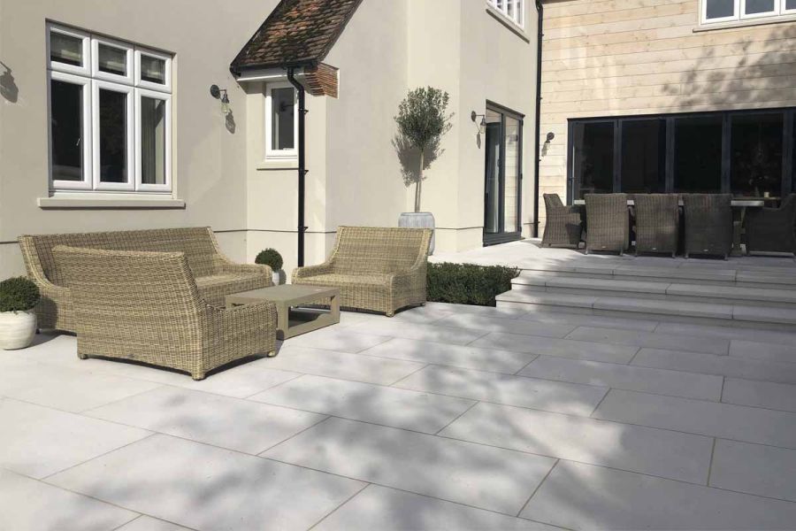 Comblanchien porcelain patio with wide garden steps leading to ratan garden furniture set located in front of bifold doors.