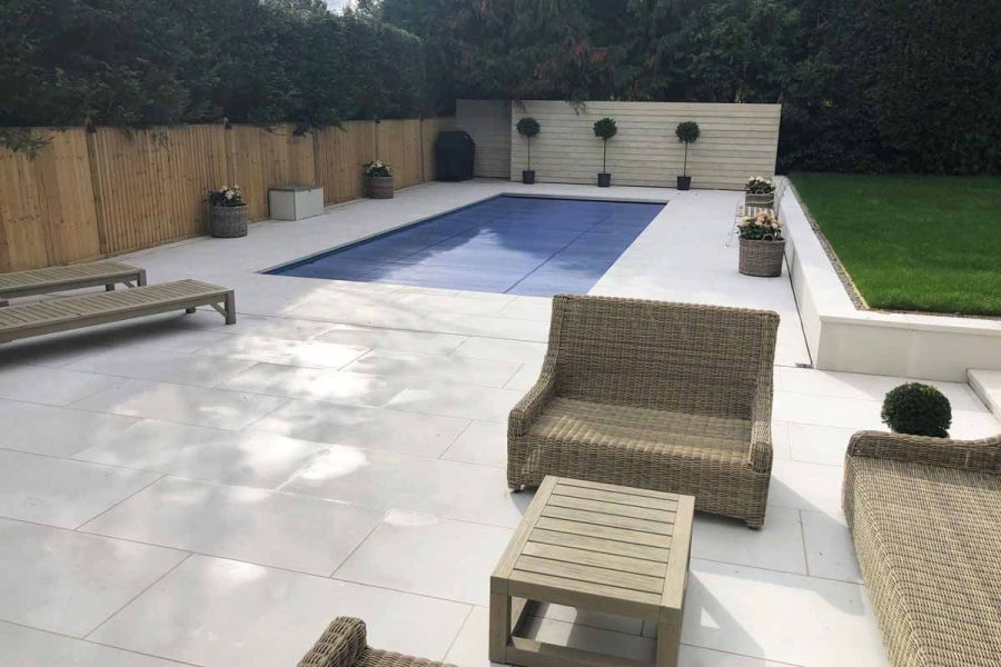 Patio slabs supplied by London Stone known as Comblanchien Porcelain Paving featured in modern garden with swimming pool.