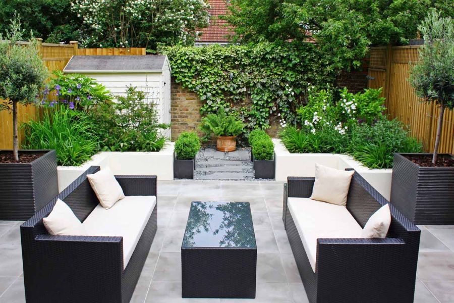 2 modern sofas face each other across table in garden paved with Contemporary Grey sawn sandstone paving, with steps up to shed.