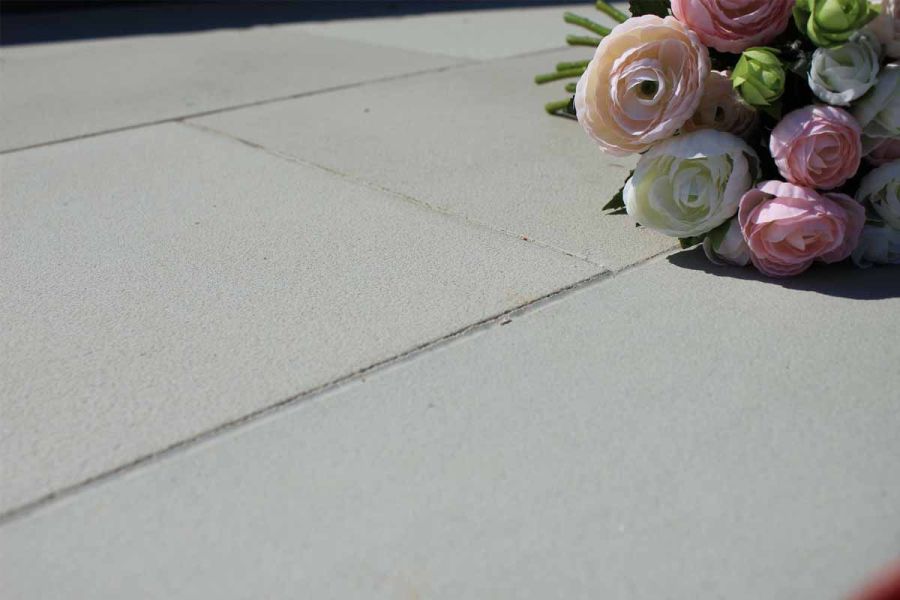 Close-up of Contemporary Grey sandstone smooth paving slabs, showing colour and sandblasted finish, with rose bouquet in background.