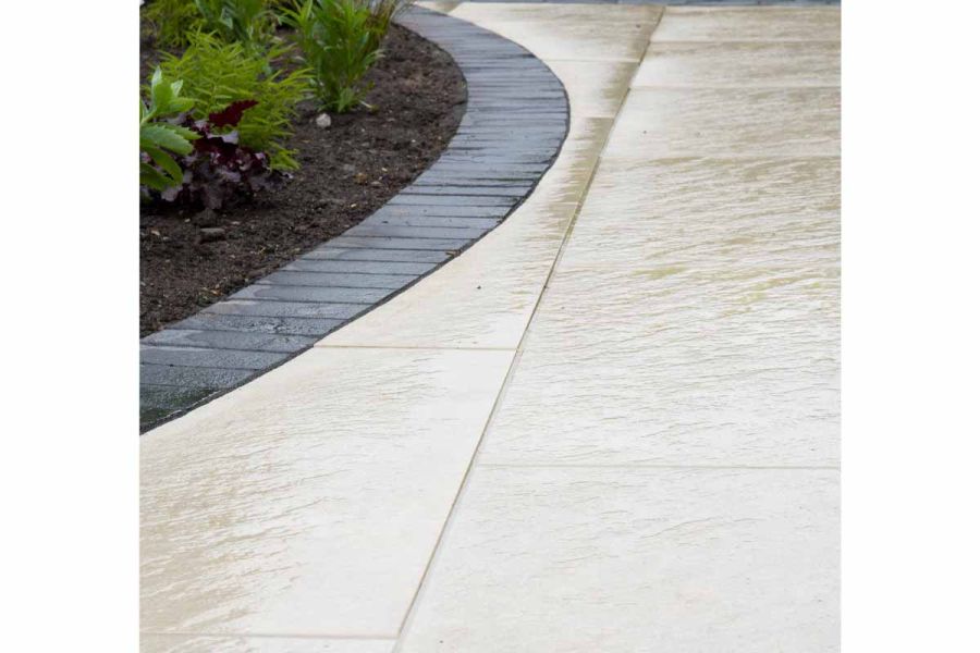 Close up shot showing texture in wet weather of Golden Stone Porcelain Paving cut into curves around a flowerbed.