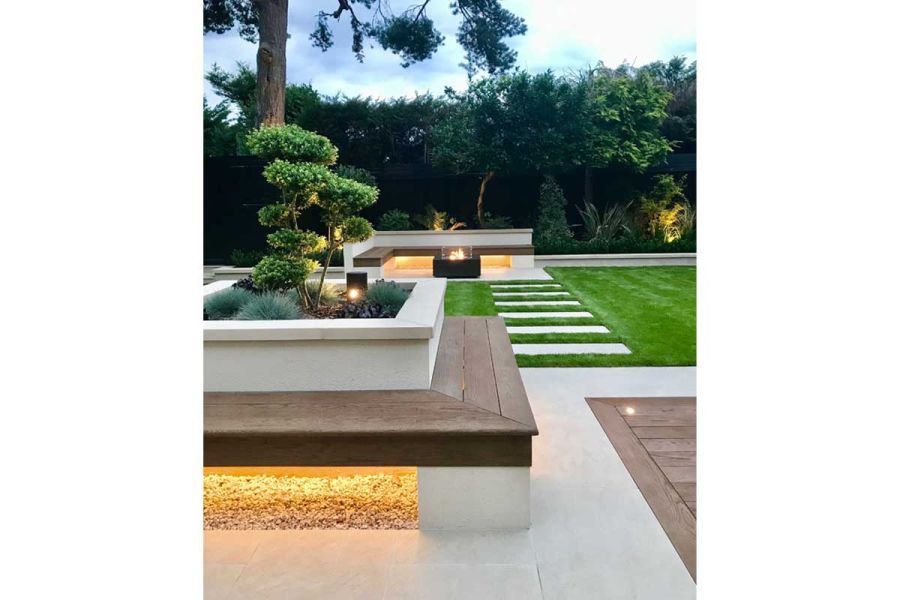 Cloud-pruned shrub in square white raised bed with underlit bench of Coppered Oak Millboard decking planks running around sides.