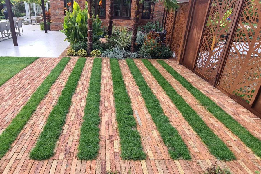 Cotswold Blend clay paver bricks laid in alternating stripes with grass, in front of pierced metal screen, next to patio.