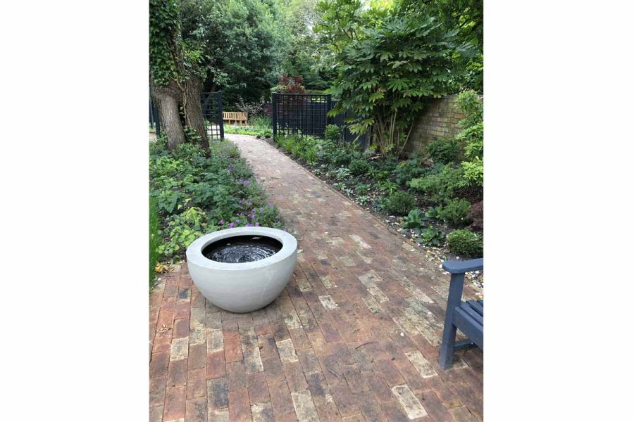 Path of Cotswold Clay Pavers between planted borders, withconcrete bowl water feature, leading to bench. Design by Eat Landscape.