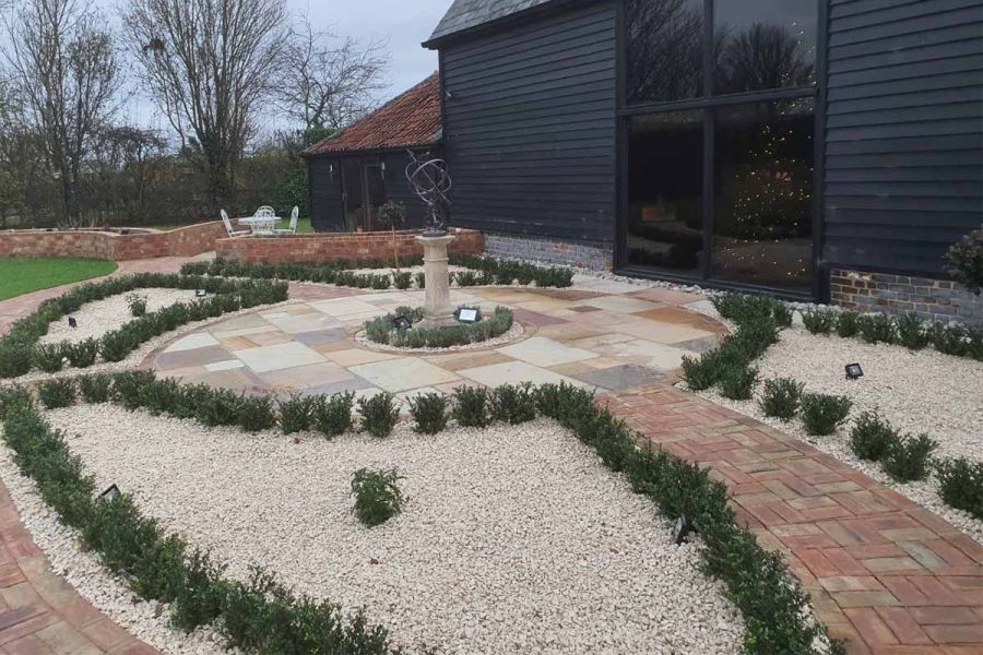 Sculpture sits on central paved circle edged by shaped gravel beds divided by Cotswold clay paver paths. Design by Floral and Hardy.