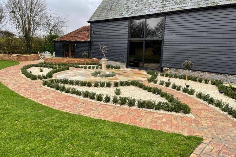 Barn conversion fronted by paths of Cotswold clay pavers outlining curved beds by metal sculpture. Design by Floral and Hardy.