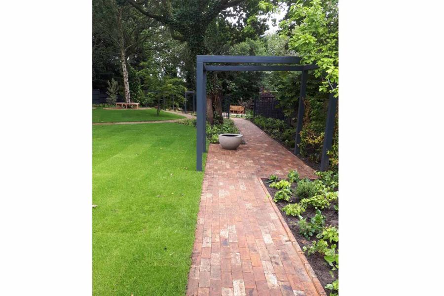 Metal pergola straddles path of Cotswold Clay Pavers between planted border and straight-edged lawn. Built by Urban Landscape.