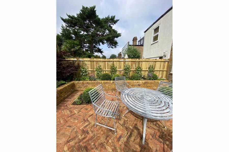 Patio of Cotswold clay paver bricks laid in mixed paving pattern of herringbone and stacked bond with metal table and chairs.