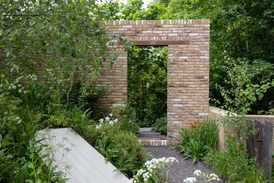 Tall arch of London Mixture Garden Wall Bricks, with wooden lintel, surrounded by trees and shrubs. Design by Paul Hervey-Brookes.
