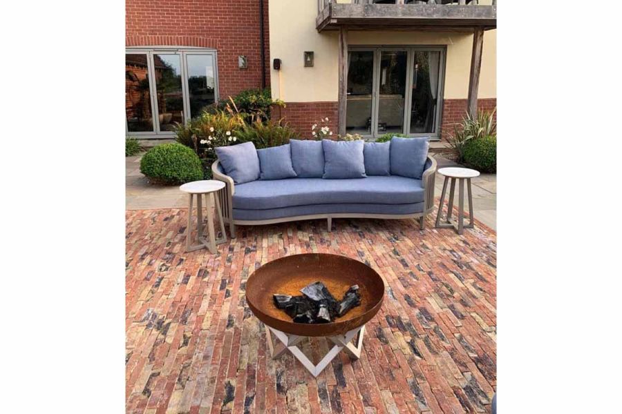 Fire bowl and blue sofa sit on Cotswold Blend clay pavers in front of cream and brick house with 2 sets of bi-fold doors.