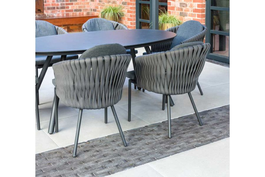 Pale outdoor porcelain tiles with wide strip of Charcoal Grey clay paving laid running bond, under oval table and 5 chairs.