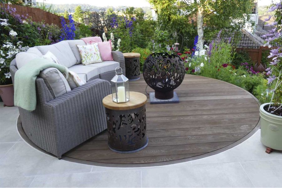 Circular Millboard decking seating area with Cream porcelain paving surround looking over sloped planted flower beds.