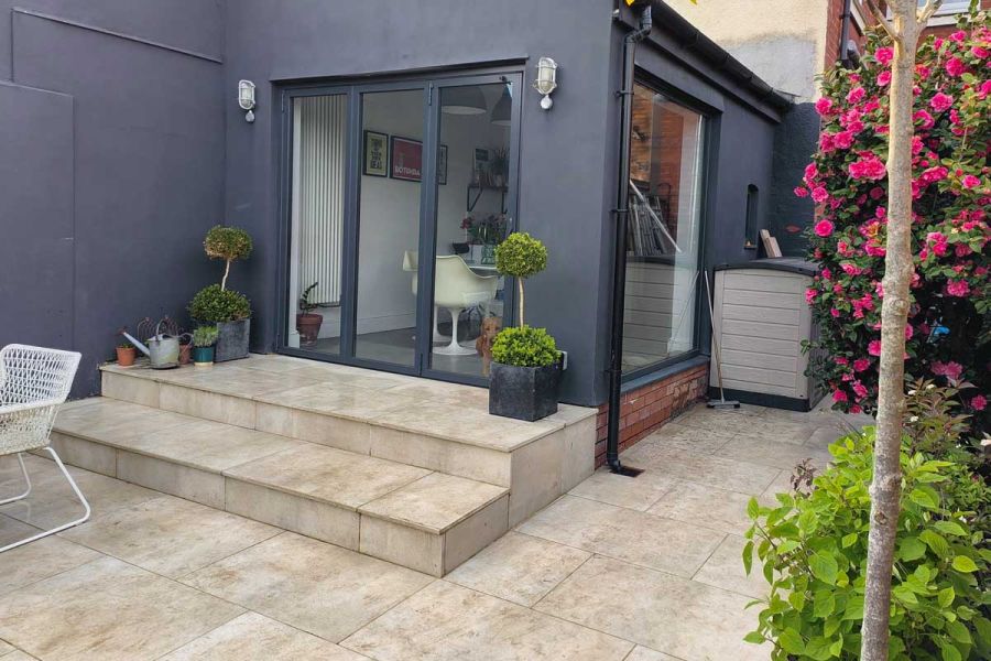 Grey kitchen extension with bi fold doors stepping down onto a Cream porcelain paved patio grouted with buff coloured grout.