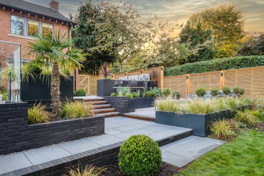 Patio on 4 levels paved in Trendy Black porcelain slabs, with raised beds and under-step lighting. Design by Creative Gardens.
