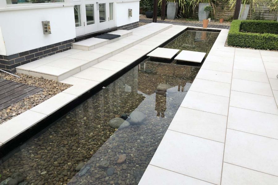 2 wide steps down from back of house to long oblong pond. 2 stepping stones cross to other side. All in Florence White porcelain.