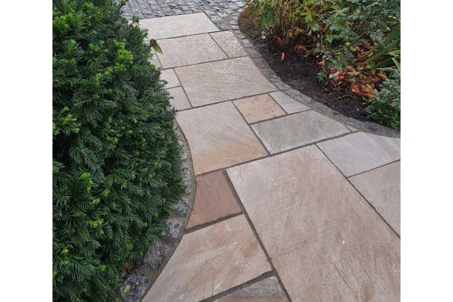 Autumn brown Indian sandstone path narrows to meet granite setts between large shrubs. Built by Cypress Garden Services.