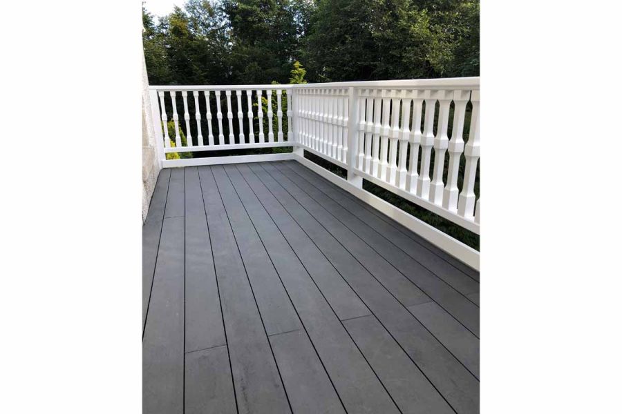 2 sides of balcony with white balustrade, laid with Dark Ash Brushed composite decking planks running lengthways. Trees behind.