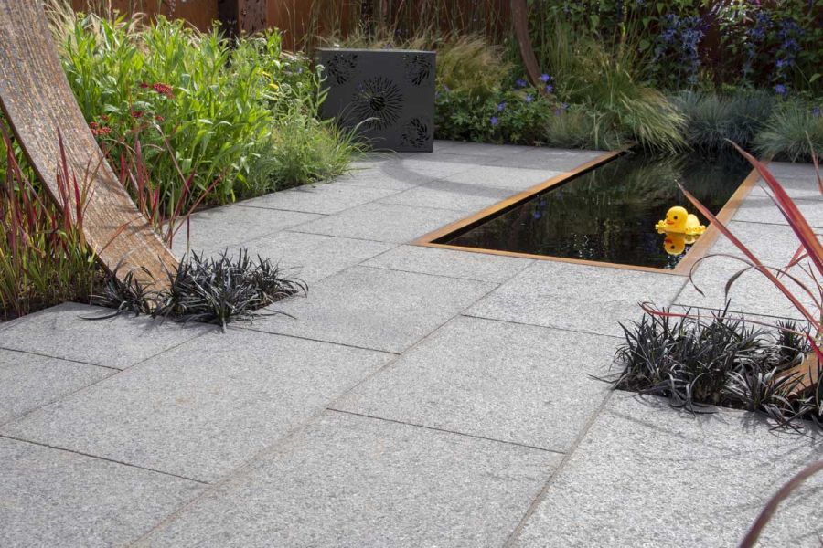 Plastic duck floats in inked oblong pond set in Dark Grey Granite slabs, built by Burnham Landscapes. RHS Hampton Court 2022.