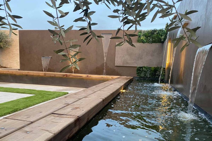 L-shaped raised pond with bench edging is fed by water spouts set into wall faced with Dark Mocha exterior cladding.