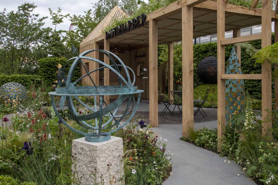 Large oak framed outdoor Pergola and garden buildig sat amongst a Trendy Grey Porcelain patio, flower bed and metal sculptures.