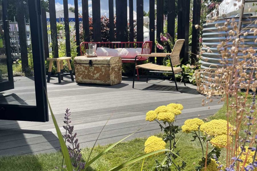Charcoal composite deck with mismatched furniture, outside open french doors on Vitamin G Garden, RHS Hampton Court 2022.