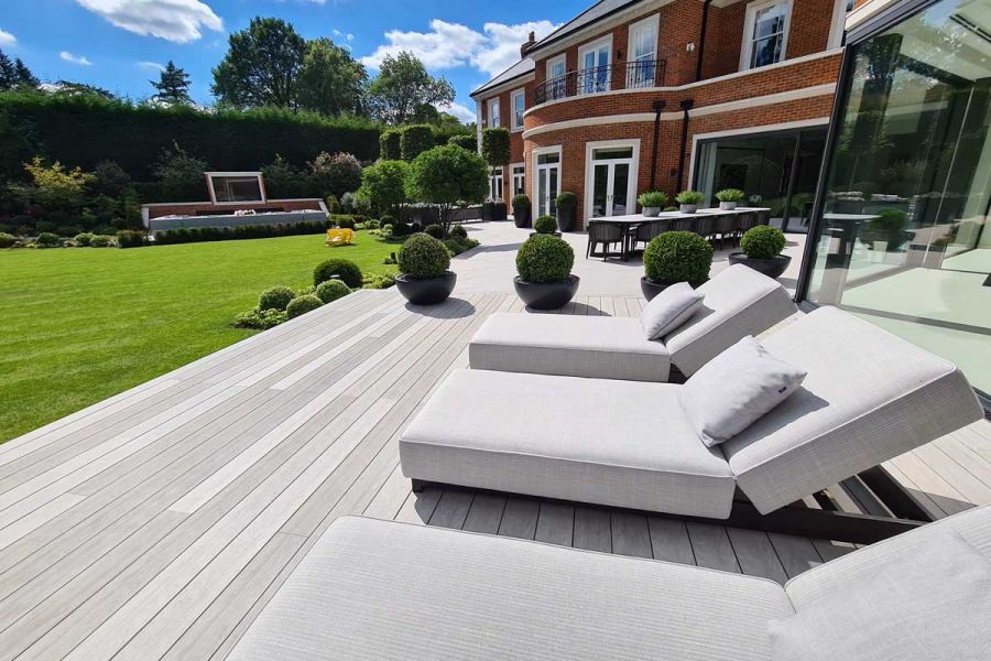 Deep-cushioned recliners on Luna decking boards, part of a patio stretched across the back of a large house. Built by Stone & Webb.
