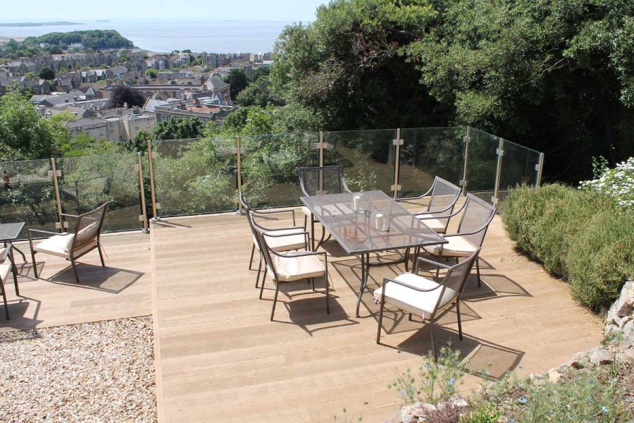 Dining set on Golden Oak Millboard decking on roof terrace overlooking view across roofs to sea. Built by Outerspace Gardens.