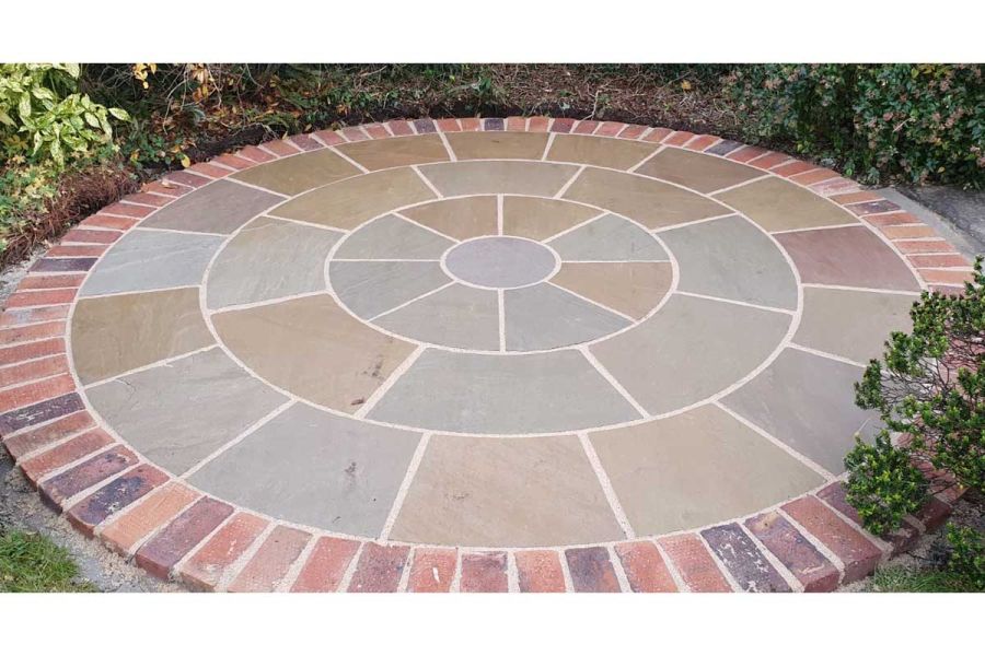 Sandstone circle fully edged by soldier course of Delta Light Multi driveway pavers, surrounded by shrubs. Built by Dorking Paving.