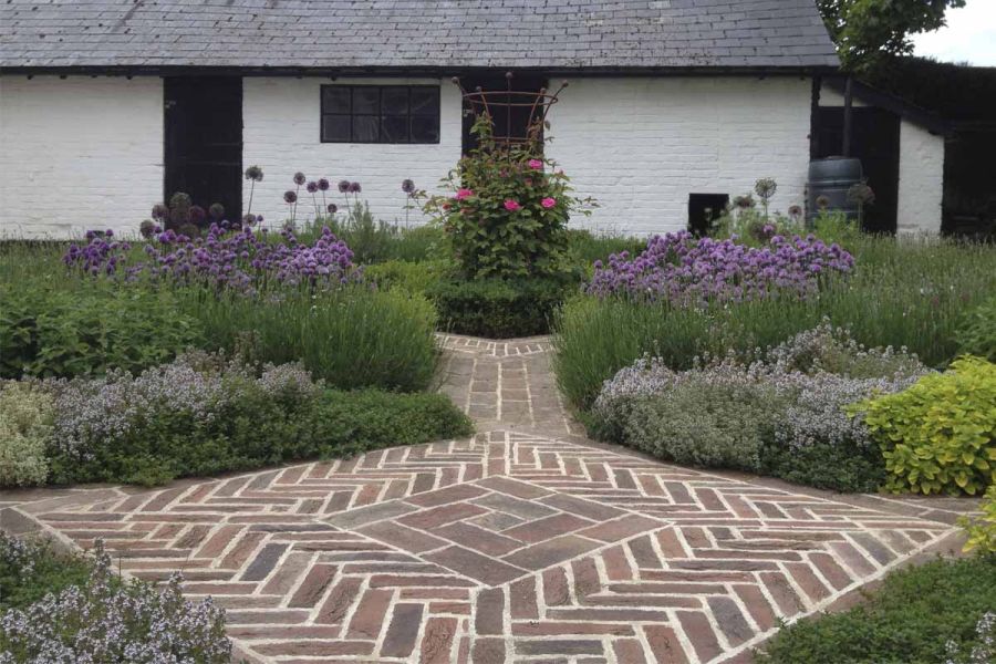 Square of Dorset Antique clay pavers designed by Helen Alison, in midst of beds of mixed herbs, paths leading away at each corner.