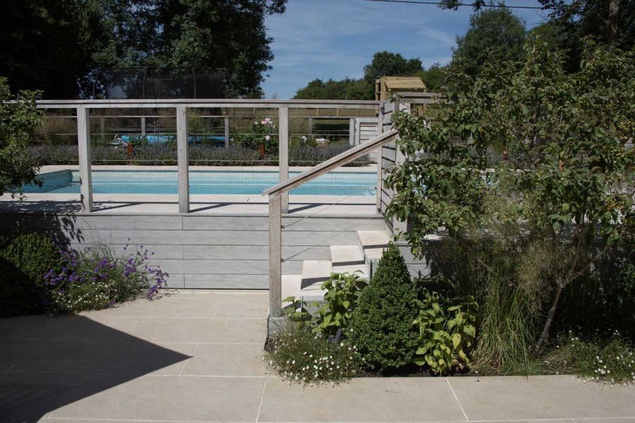 Small Porcelain patio with steps leading up to a raised swimming pool surrounded by mature planting.