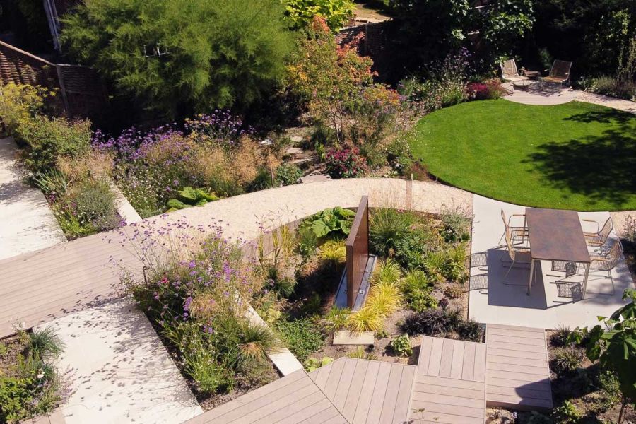 Round lawn and planted beds are backdrop to path from Traditional DesignBoard composite decking path to patio. Design by D Holloway.