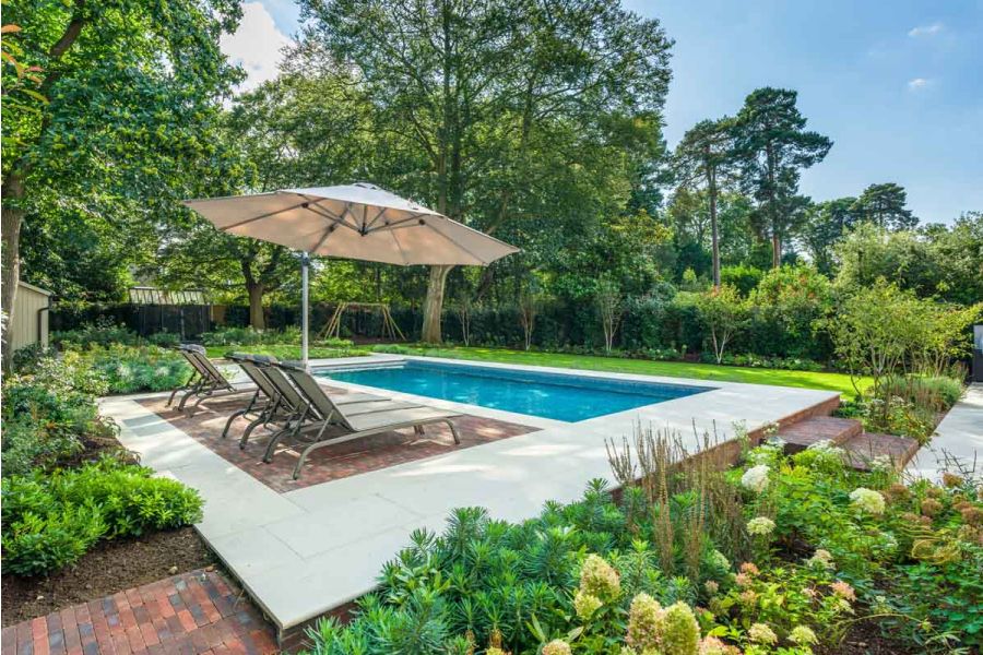 Large garden with trees, lawn, borders, and swimming pool, with sunloungers on Dove Grey Smooth Sandstone paving and clay pavers.