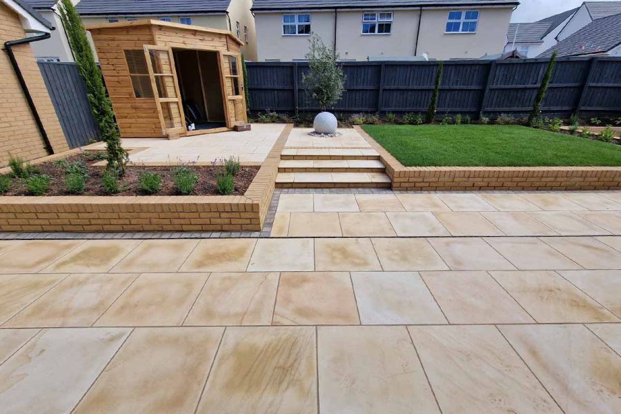 wide shot of large garden with outhouse, water feature and raised flowerbeds. Dune smooth sandstone shows off its veining in large patio.