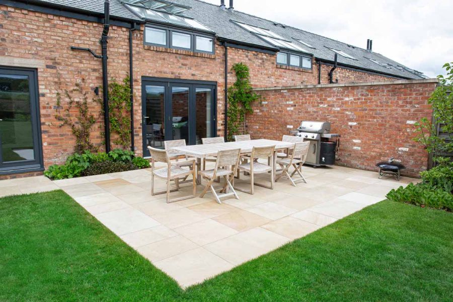 Large rectangular Dune Smooth sandstone patio with 8-seater dining table in corner created by wall and house with bi-fold doors.