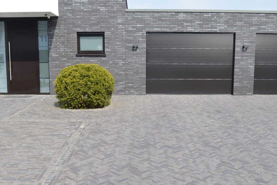 Area outside front of grey house with 2 garages completely paved in matching Carbona Belgian bricks laid in different patterns.