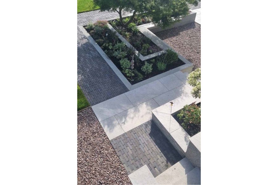 Clean cut porcelain slabs surrounded by pebbles, with chunks of Lugano Dutch Clay Pavers between flowerbeds.