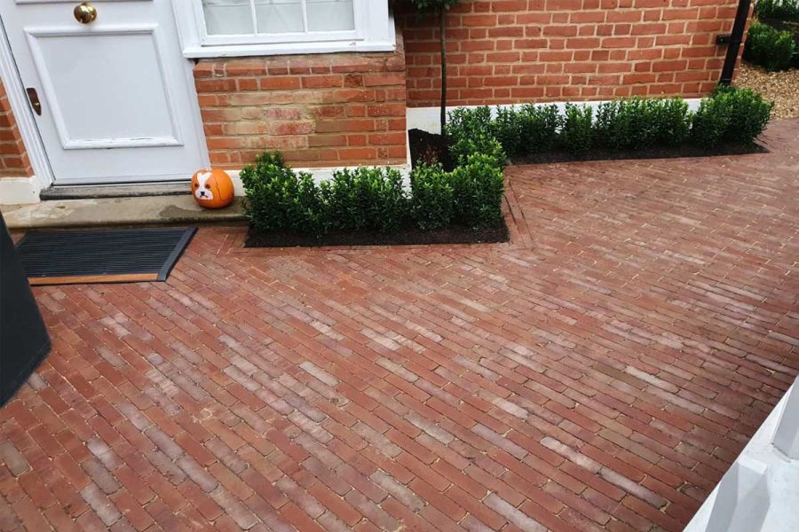 Roma Clay Pavers laid across front of house. Bed with low hedging follows angles of building’s wall. Design by AS Landscapes.