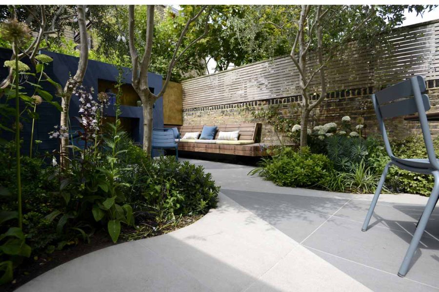 Remarkable courtyard garden showcasing trendy black and urban grey porcelain arranged in angular designs, bordered by fencing and trees to ensure privacy.