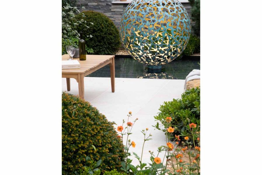 Garden at RHS Malvern Flower Show, with Egyptian Beige Limestone paved area next to pond with large pierced metal ball lit within.