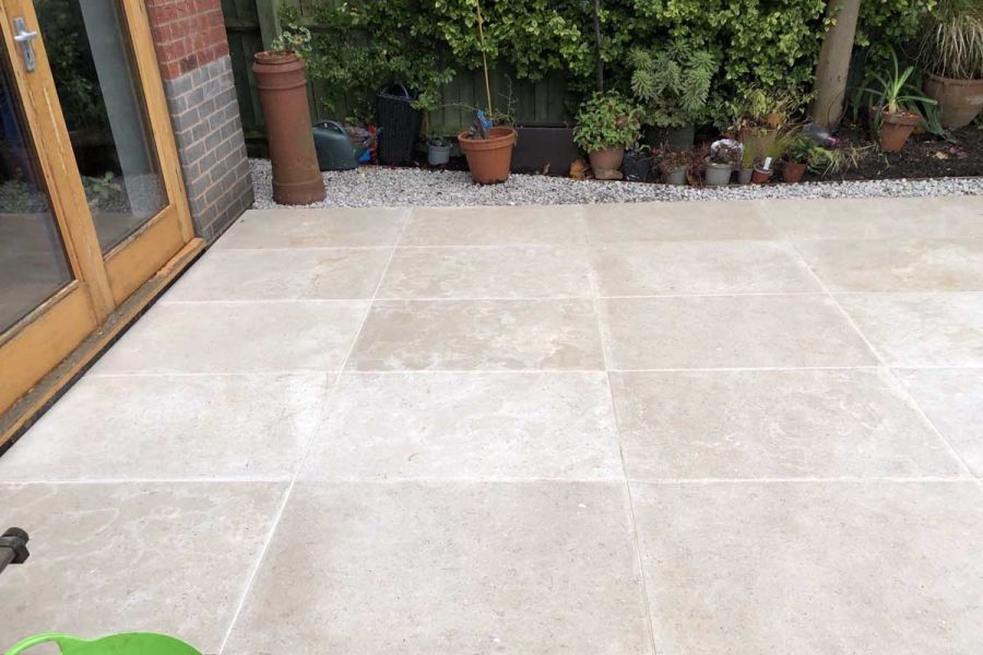 Egyptian beige limestone paving laid stack bond with light-coloured pointing, by french doors, edged with gravel and planted pots.