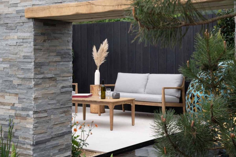 Next to pond, outdoor sofa and table sit on Egyptian Limestone paving, viewed through flat-topped arch clad in Graphite Sandstone.