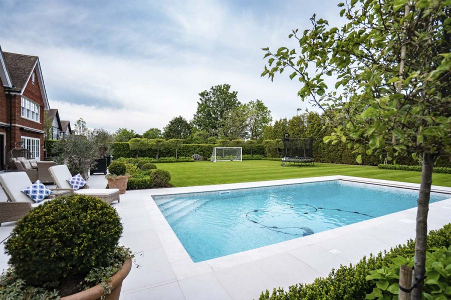 Blue-lined swimming pool surrounded by Florence Grey Premium porcelain paving at end of matching patio, designed by Elitescapes.