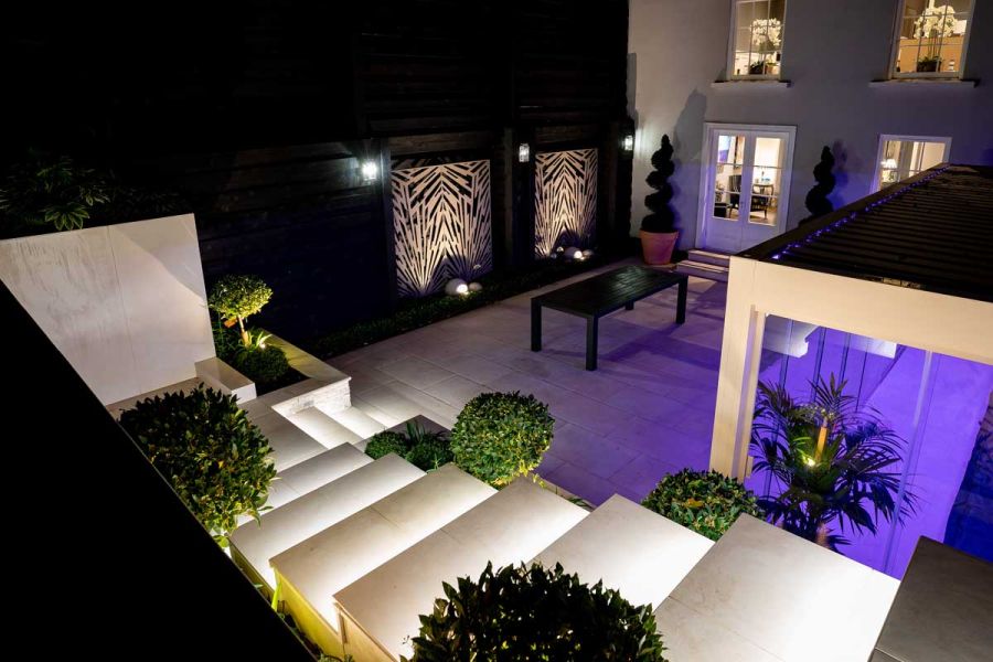 Set of beige porcelain steps heading down into a stylish paved basement garden featuring a large white Pergola.
