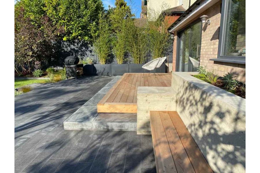 Patio of Black granite plank paving across back of house, with 2 steps up to wooden deck outside bi-fold doors.