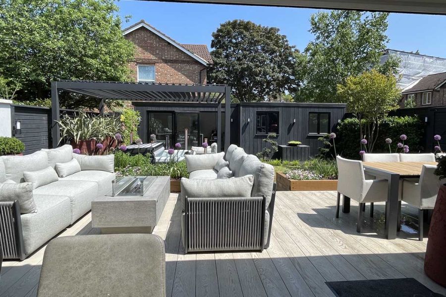 Composite deck with outdoor furniture, Proteus Grey aluminium pergola and garden buildings in background. Built by Olive Tree.