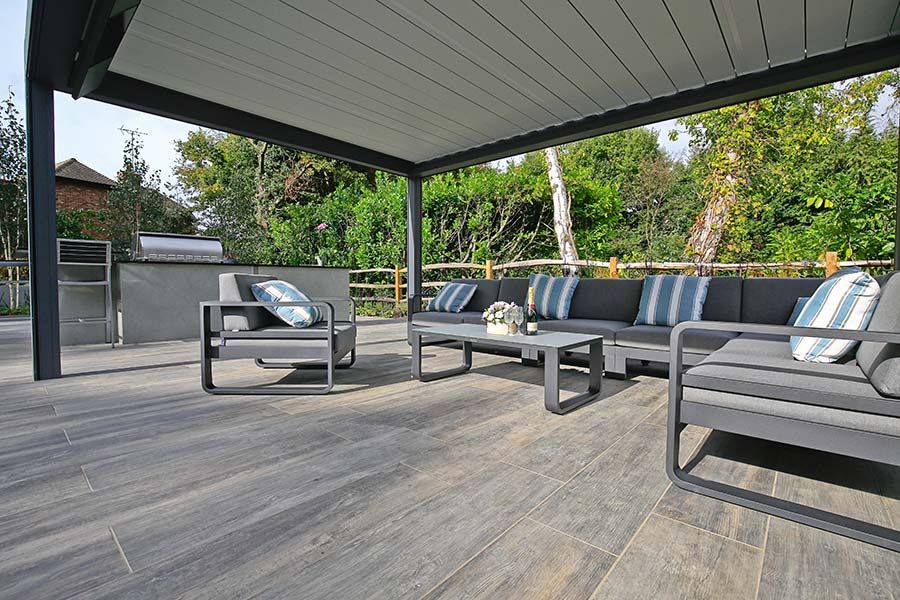 Wood Effect Porcelain paving slabs laid in planks underneath a large Renson pergola with grey garden lounging set.
