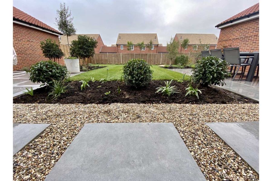 Anthracite 800x800 porcelain slabs set in gravel at head of rectangular lawn with planted bed. Design by Essex Garden Designs.