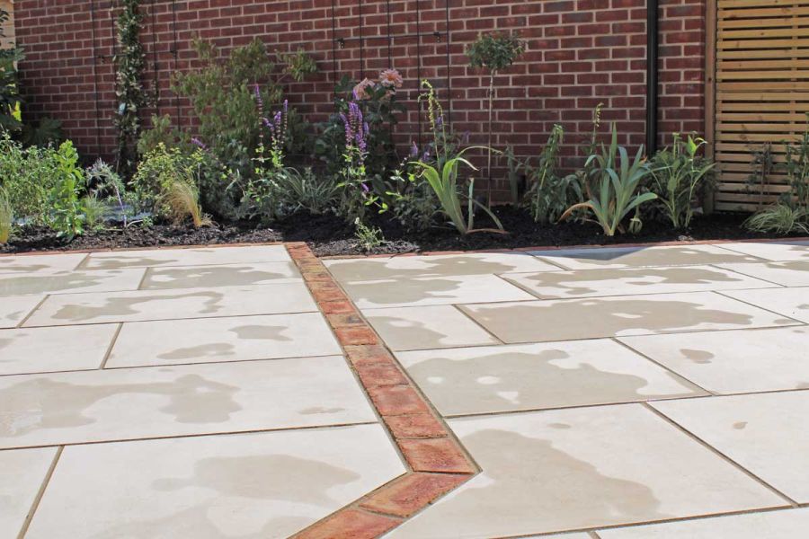 Wall with planted border by Venetian Beige porcelain paving with step with clay paver edge detail. Built by Essex Garden Designs.