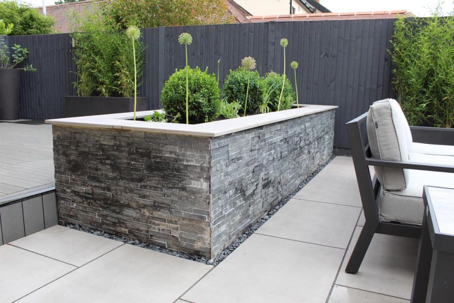 Large raised planter bed clad with slate cladding and capped with a Polished Grey porcelain paving slab.